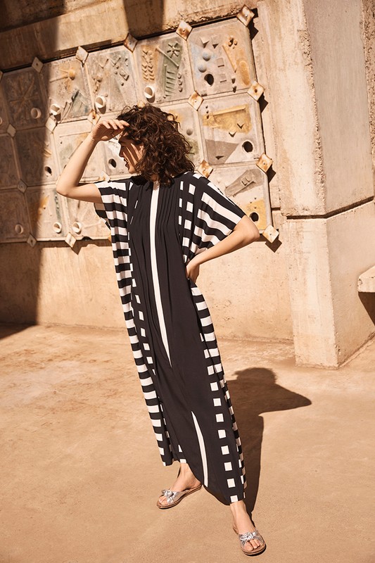 Adult female poses outdoors wearing a striped black and white dress. The woman is standing near a tiled wall.