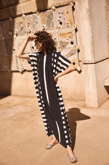 Adult female poses outdoors wearing a striped black and white dress. The woman is standing near a tiled wall.