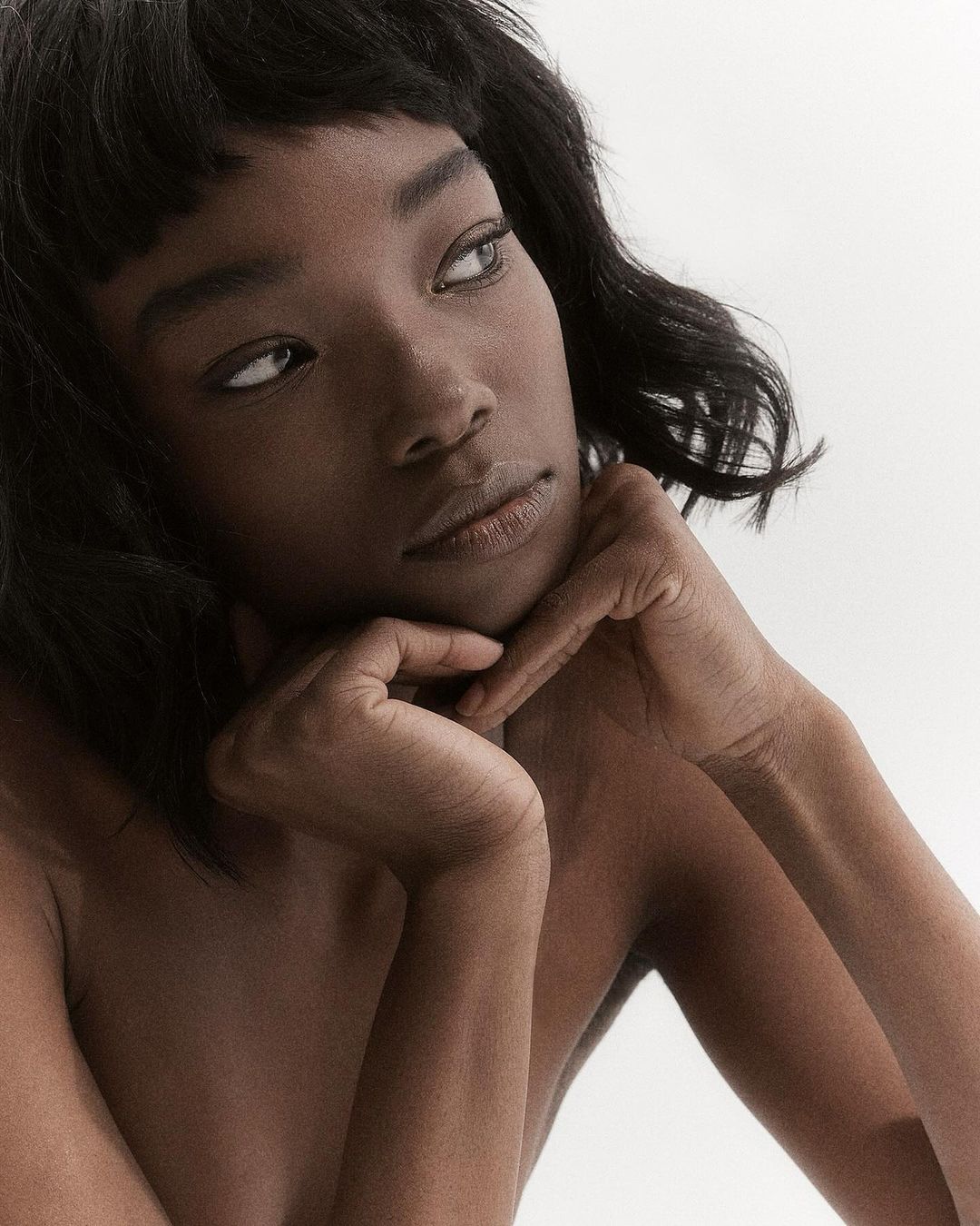 Close-up portrait of an African American adult female with short dark hair, resting her chin on her interlaced fingers, looking off to the side.