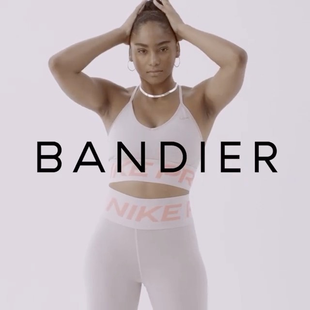 Woman in sportswear poses with hands on head in a studio shot for athletic apparel brand Bandier wearing Nike apparel in front of a white backdrop.