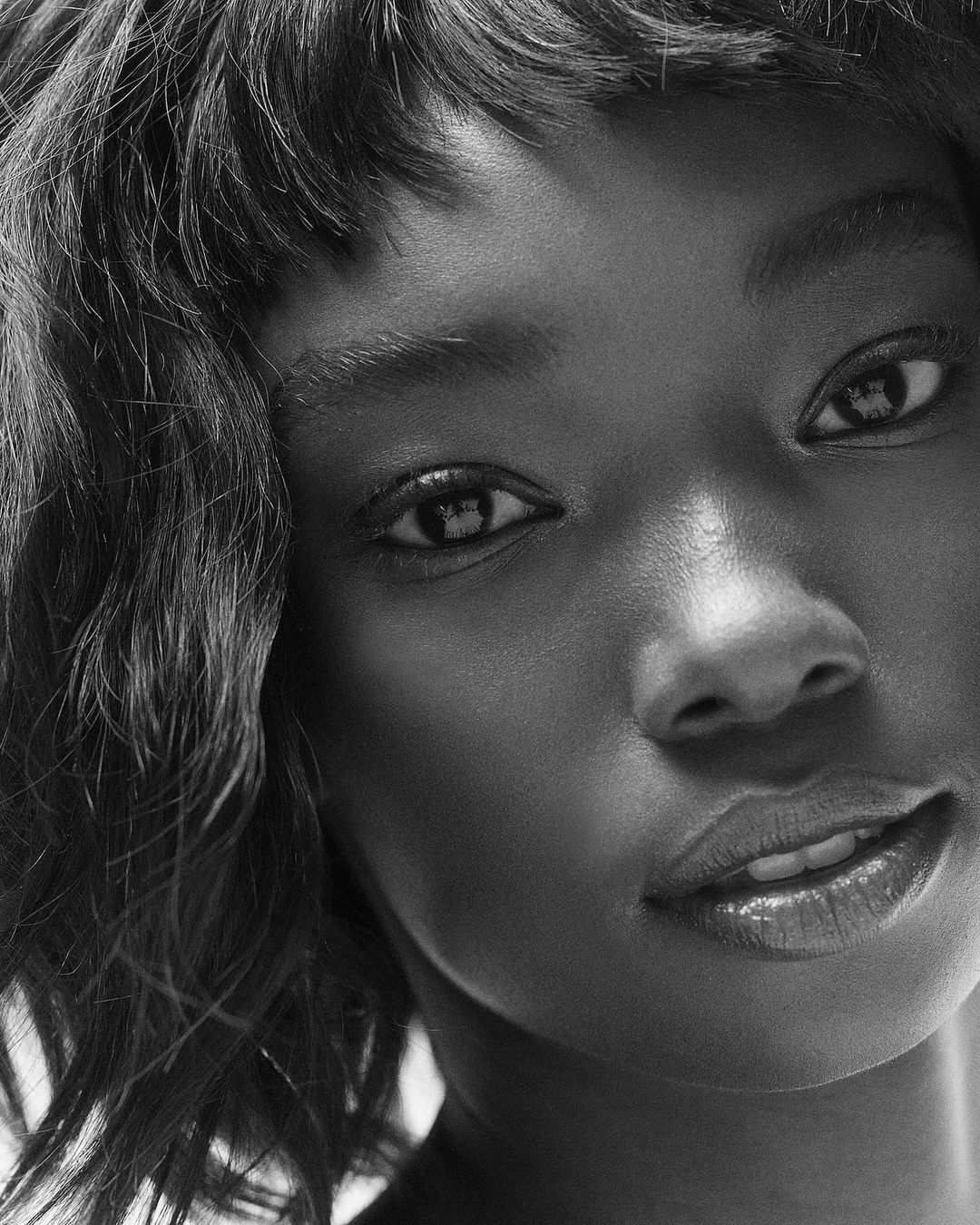 Close-up studio portrait of an African-American adult female with curly hair looking at the camera in black and white.
