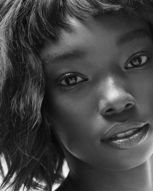 Close-up studio portrait of an African-American adult female with curly hair looking at the camera in black and white.