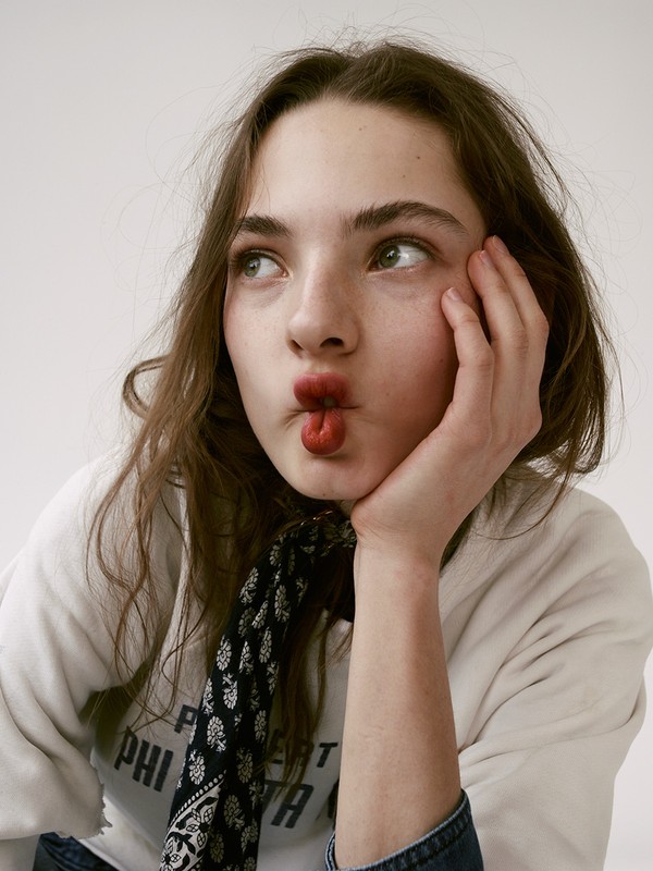 Portrait of a young woman with brown hair, wearing a white sweatshirt and black and white bandana, puckering her lips in a funny expression.
