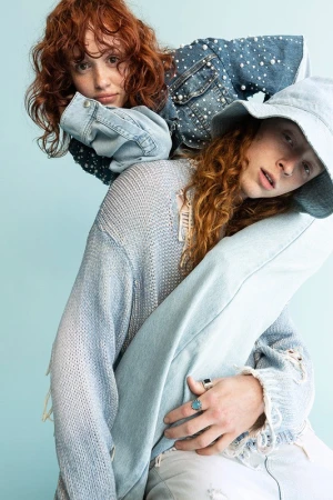 Two red-haired models in denim attire, styled by Lara Backmender against a pale blue background.