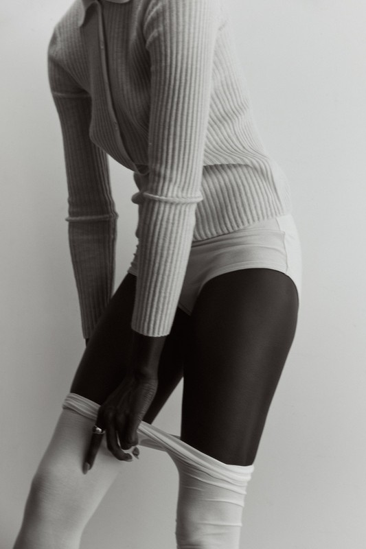 Model wearing a ribbed top and light-colored hosiery against a seamless white studio background styled by Lara Backmender.