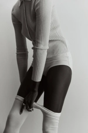 Model wearing a ribbed top and light-colored hosiery against a seamless white studio background styled by Lara Backmender.
