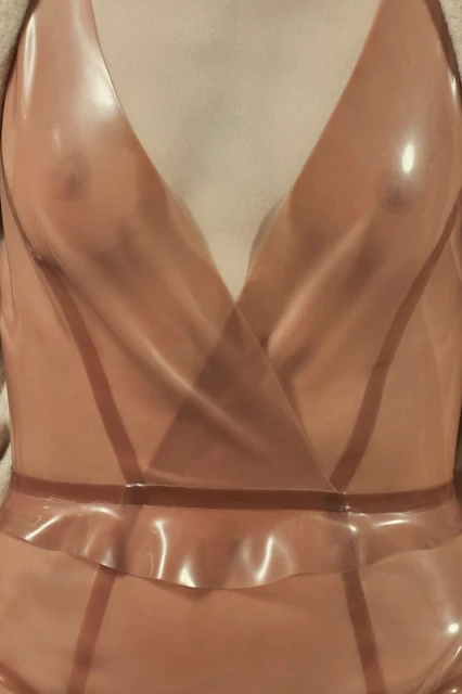 Close-up studio shot of a female torso in a peach-colored, transparent, fitted latex bodysuit with a plunging neckline, cinched waist, and shoulder pads.