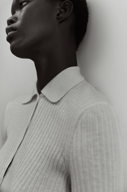 Close-up of a Black female model in a light gray ribbed collared shirt against a light gray background, highlighting the shirt's texture.