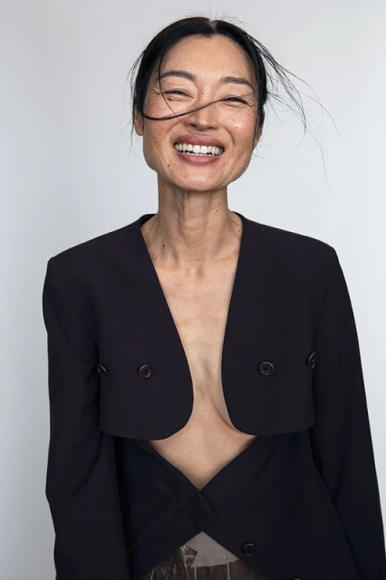 Close-up portrait of smiling adult woman with black hair wearing a black blazer against a white background in a studio setting.