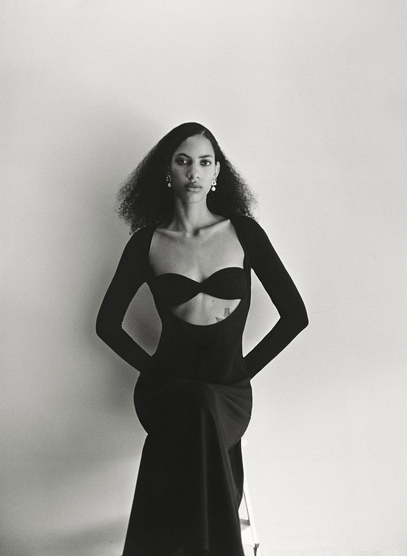 Elegant studio portrait of a woman wearing a black dress, seated and posing against a neutral background, showcasing fashion and style.