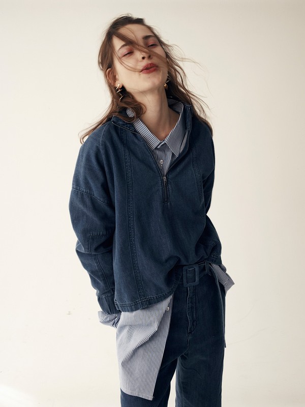 Woman in blue denim jacket and pants poses in a fashion shot in front of a white background indoors in a studio with natural light.
