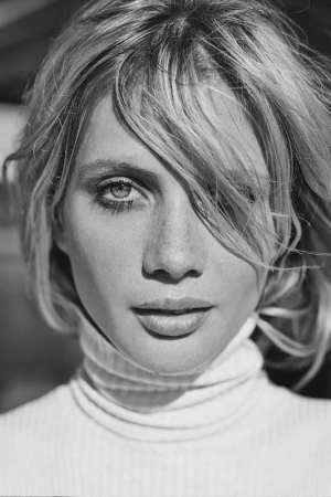 Close-up monochrome portrait of a woman wearing a turtleneck sweater with tousled blonde hair covering part of her forehead.