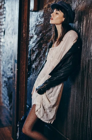 Woman in white dress and black jacket leaning against a textured brick wall in Los Angeles