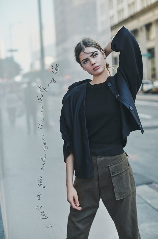 A young woman in a jacket and cargo pants poses against a city backdrop. Urban fashion portrait with soft lighting and street scene.