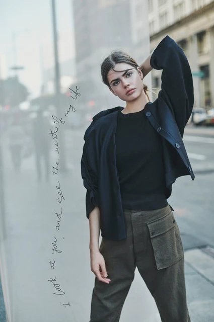 A young woman in a jacket and cargo pants poses against a city backdrop. Urban fashion portrait with soft lighting and street scene.