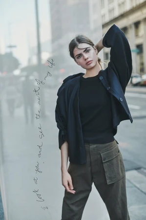 A young woman in a jacket and cargo pants poses against a city backdrop. Urban fashion portrait with soft lighting and street scene.