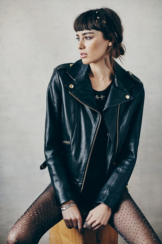 Portrait of a woman with dark hair and a black leather jacket, looking off-camera with a neutral expression against a neutral backdrop.