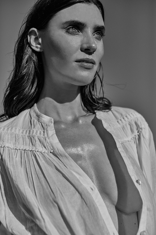 Monochrome portrait of a fair-skinned woman with dark hair wearing an unbuttoned white blouse, looking up and away from the camera.