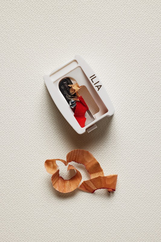 Close-up of an Ilia beauty pencil sharpener with shavings, set against a textured cream background in a simple studio shot.