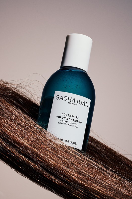 SACHAJUAN Ocean Mist Volume Shampoo bottle with white cap on a strand of highlighted brown hair, against a light beige background.