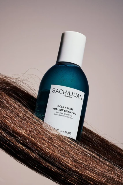 SACHAJUAN Ocean Mist Volume Shampoo bottle with white cap on a strand of highlighted brown hair, against a light beige background.