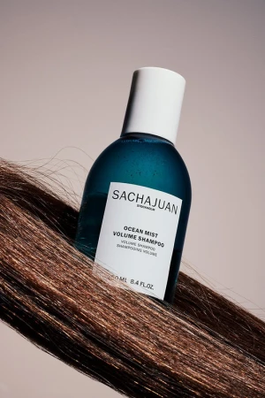 SACHAJUAN Ocean Mist Volume Shampoo bottle with white cap on a strand of highlighted brown hair, against a light beige background.