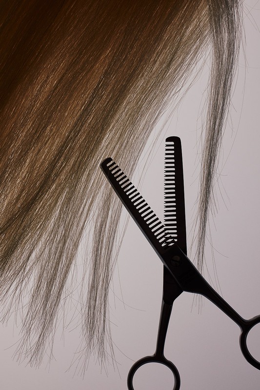 Close-up studio shot of brown hair being cut with thinning shears against a pale background, creating a beauty and haircare image.