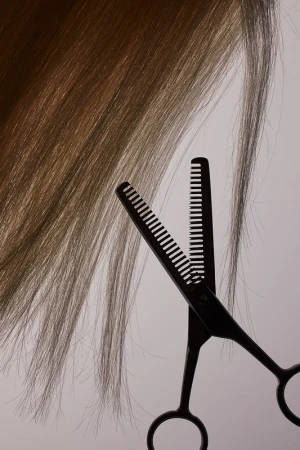 Close-up studio shot of brown hair being cut with thinning shears against a pale background, creating a beauty and haircare image.