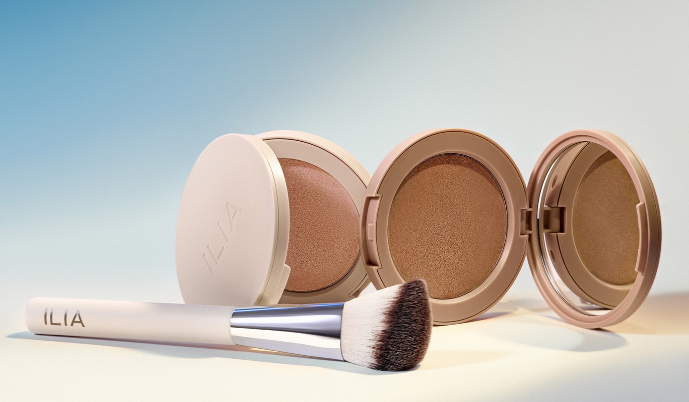 Cosmetic product flat lay: powder compacts and makeup brush against a soft gradient blue and beige background.