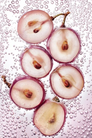 Close-up of sliced red grapes suspended in sparkling water with bubbles against a light background, showing seeds and juicy texture.