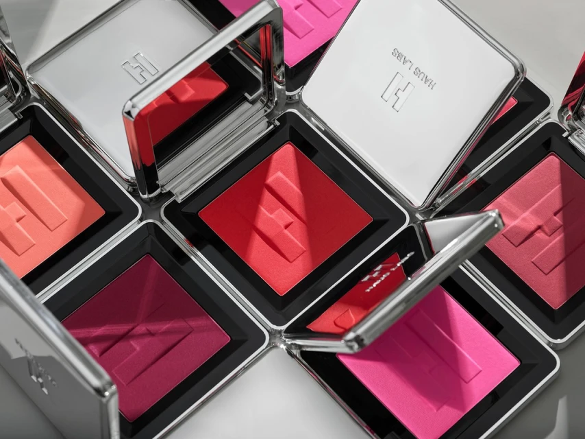 Multiple square compacts of Haus Labs blush in various shades, arranged diagonally, feature silver cases with mirrored lids and embossed logo.