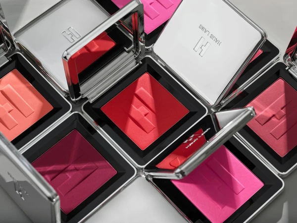 Multiple square compacts of Haus Labs blush in various shades, arranged diagonally, feature silver cases with mirrored lids and embossed logo.