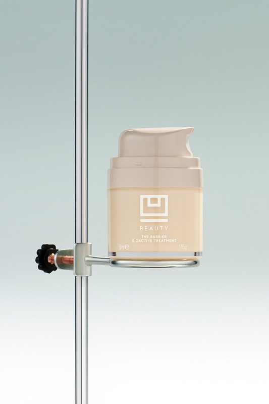 Beauty product in light beige container with pump on metal stand in studio setting, product shot for skincare advertising.