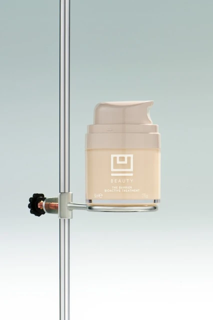Beauty product in light beige container with pump on metal stand in studio setting, product shot for skincare advertising.