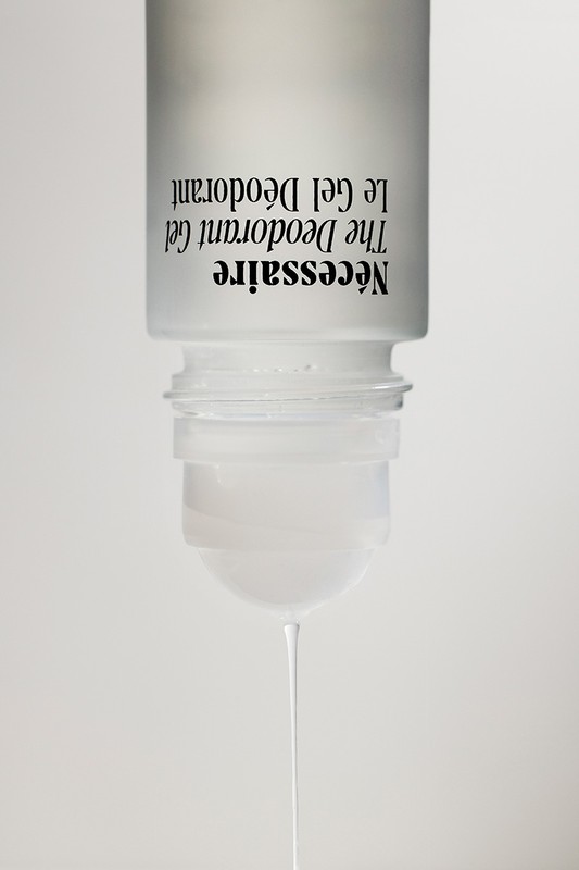 Minimalist product shot of clear deodorant gel dripping from a white bottle against a neutral background. Beauty and personal care.