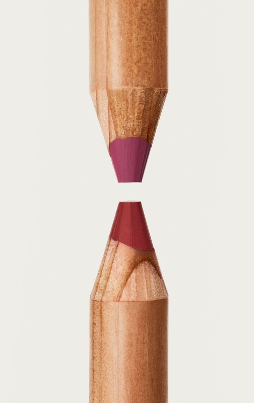 Close-up studio shot of two sharpened wood cosmetic pencils with purple and red pigment tips facing each other on a plain light background.