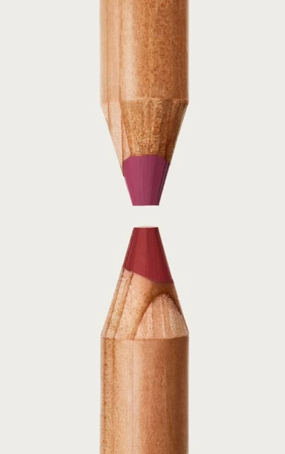 Close-up studio shot of two sharpened wood cosmetic pencils with purple and red pigment tips facing each other on a plain light background.