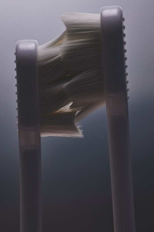 Close-up of a white toothbrush head with worn bristles against a light gray background, showcasing wear and texture detail.