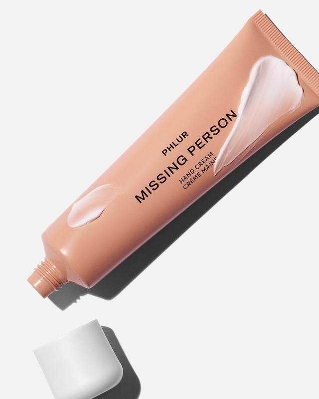 A beige tube of PHLUR Missing Person hand cream with a white dollop, alongside its white cap, against a white background.