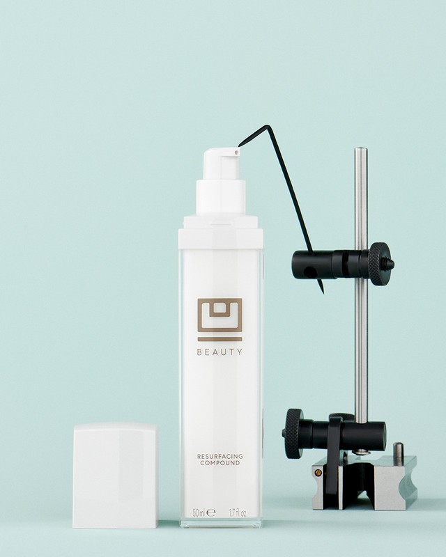 Studio product shot of white pump bottle with silver accents and white cap, displayed with a technical gauge against blue background.
