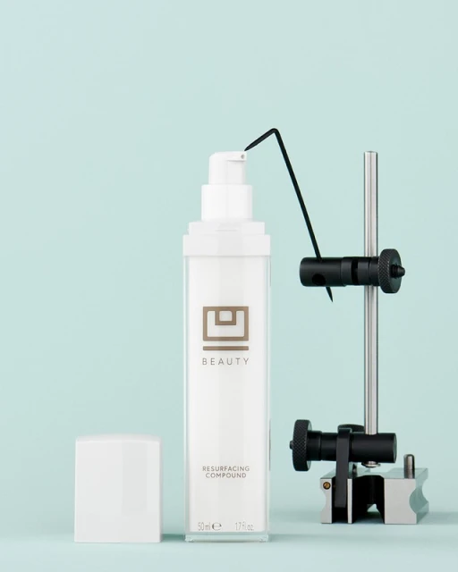 Studio product shot of white pump bottle with silver accents and white cap, displayed with a technical gauge against blue background.