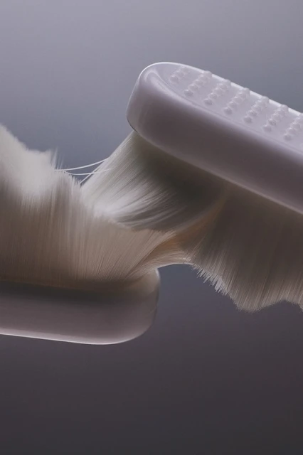 Close-up studio shot of a white, soft-bristled toothbrush head against a grey gradient background, highlighting the fine bristles and texture.