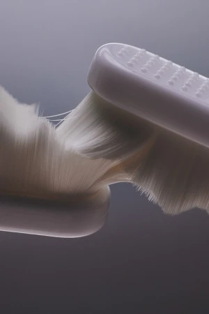 Close-up studio shot of a white, soft-bristled toothbrush head against a grey gradient background, highlighting the fine bristles and texture.