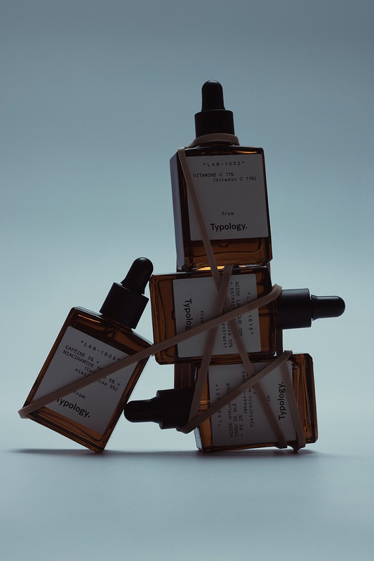 Several amber glass bottles with droppers are stacked and held together by rubber bands on a gradient white background.