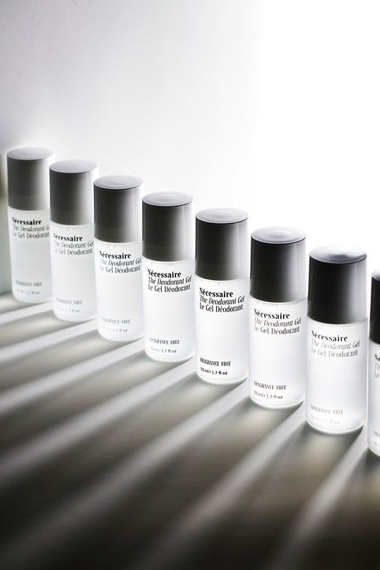 Multiple bottles of Nécessaire The Deodorant Gel lined up against a bright white background, casting sharp, dark shadows on the surface.