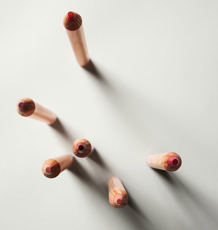 Overhead shot of a collection of colored pencils with pale wooden shafts and red cores, arranged against a light grey background.