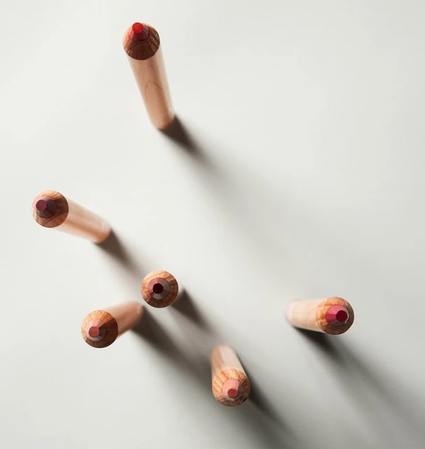 Overhead shot of a collection of colored pencils with pale wooden shafts and red cores, arranged against a light grey background.