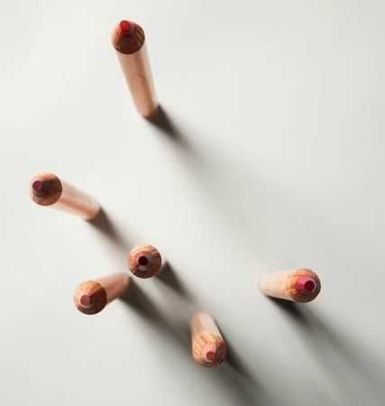 Overhead shot of a collection of colored pencils with pale wooden shafts and red cores, arranged against a light grey background.