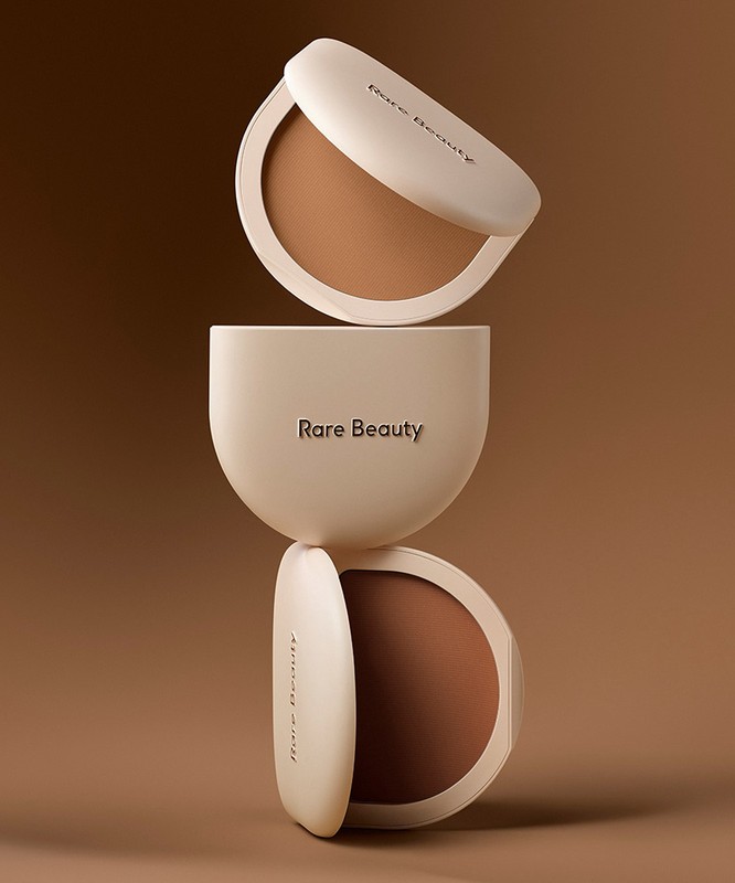 Three Rare Beauty bronzer compacts stacked on a brown background in studio lighting showcase the brand's makeup product.