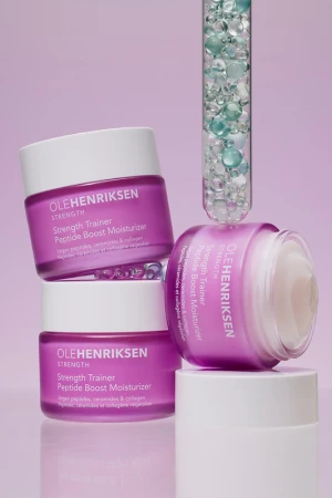 Ole Henriksen skincare product presentation. Three purple and white jars are stacked, and a test tube filled with small spheres is placed.